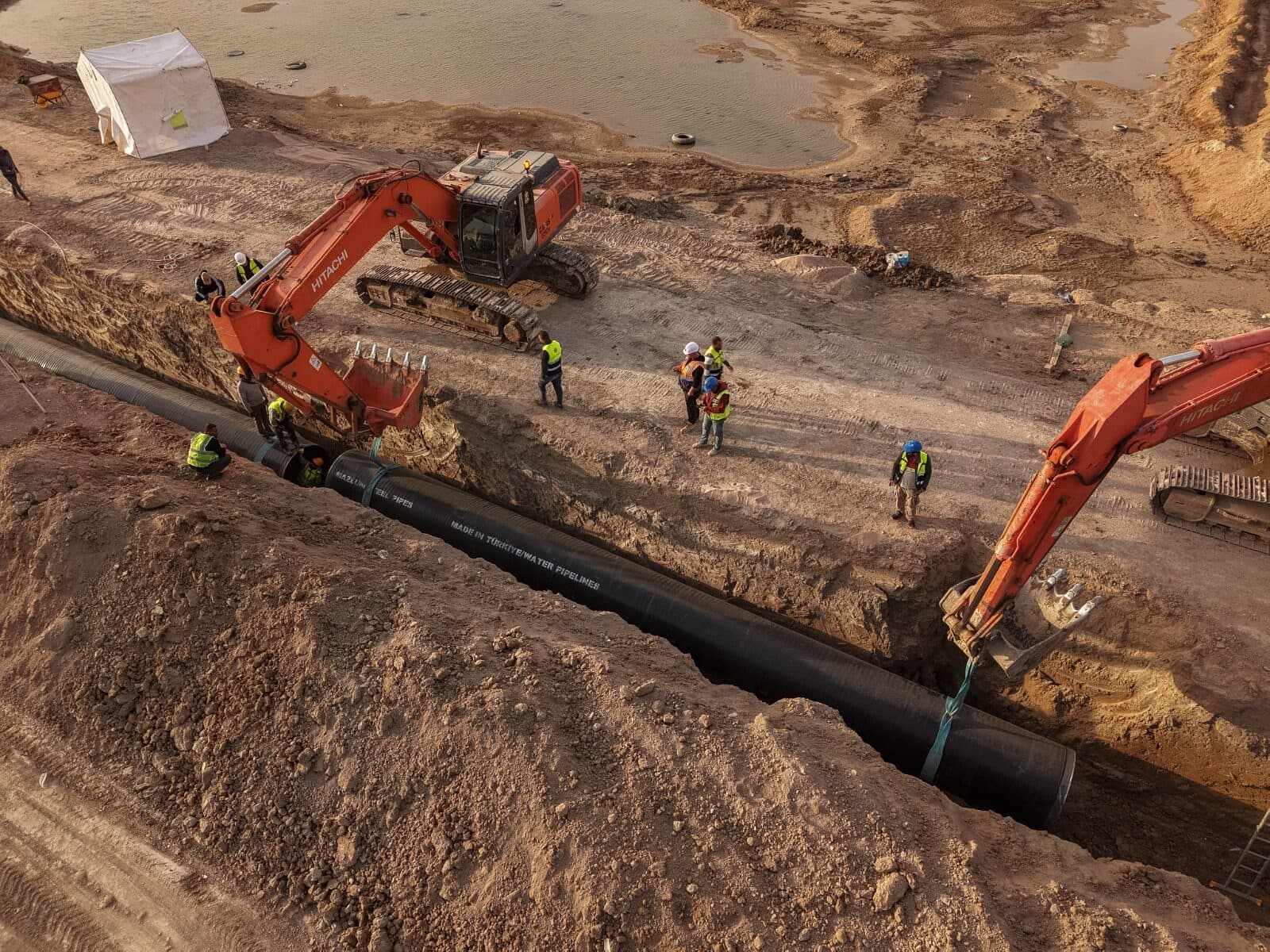 Excavators laying large pipe in trench